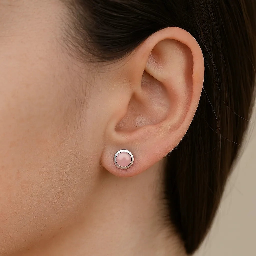Frau trägt einen Ohrstecker aus 925er Sterlingsilber mit rundem, zart roséfarbenem Rosenquarz-Cabochon. Der elegante Ohrring sitzt dezent am Ohrläppchen und unterstreicht einen femininen, zeitlosen Look.