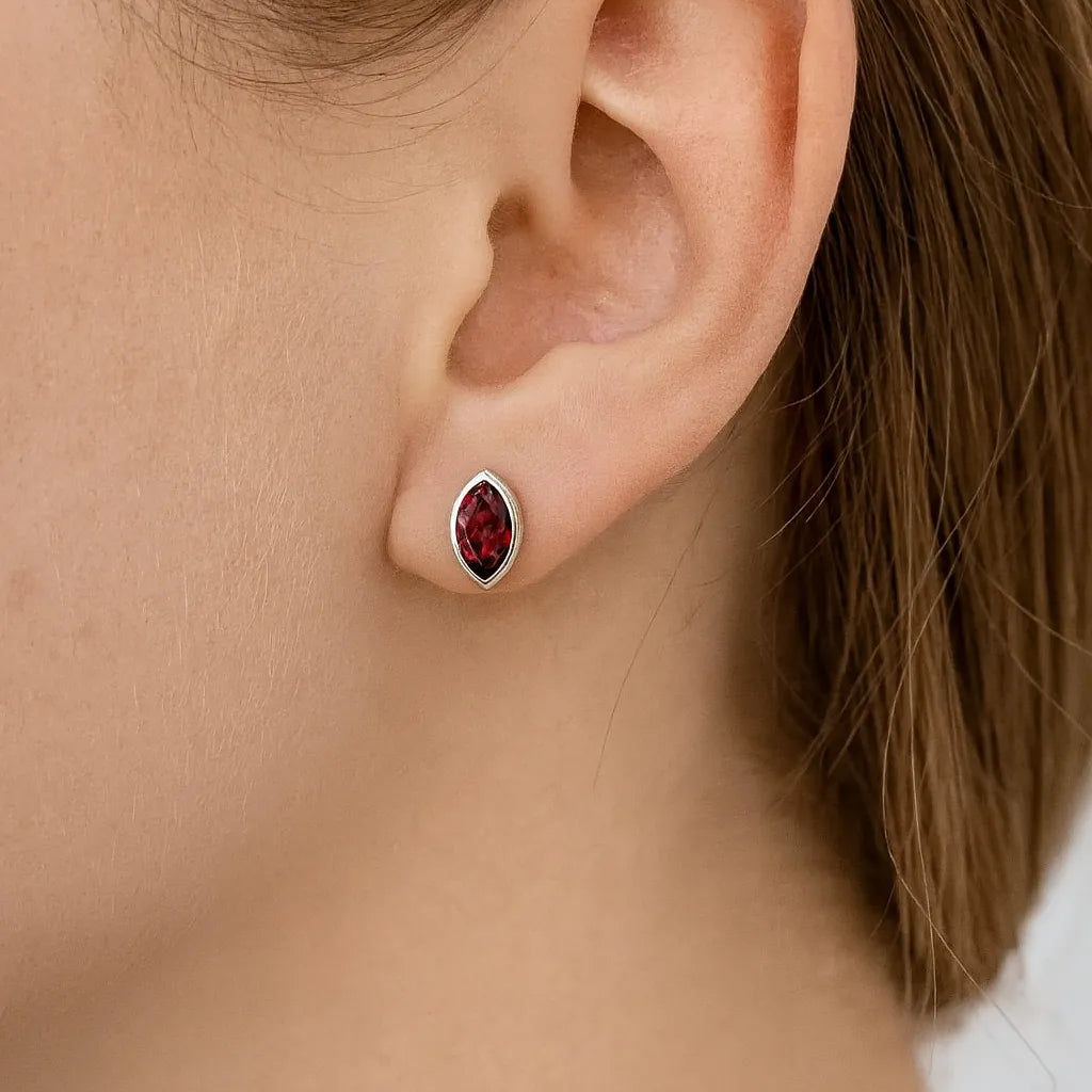 Nahaufnahme eines Ohrs mit einem eleganten Ohrstecker aus Sterlingsilber, besetzt mit einem marquisförmigen, tiefroten Granatstein in glänzender Fassung. Der Schmuck verleiht dem Look eine edle und zugleich moderne Note.
