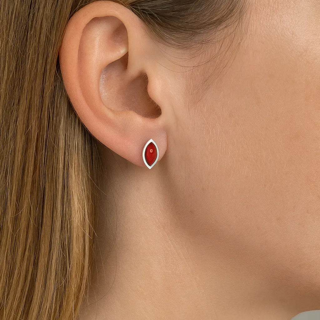 Nahaufnahme eines Ohrs mit einem eleganten Ohrstecker aus 925er Sterlingsilber und rotem Korallen-Cabochon in Marquiseform. Der Ohrstecker schimmert dezent und wirkt als stilvoller Farbakzent auf der Haut.
