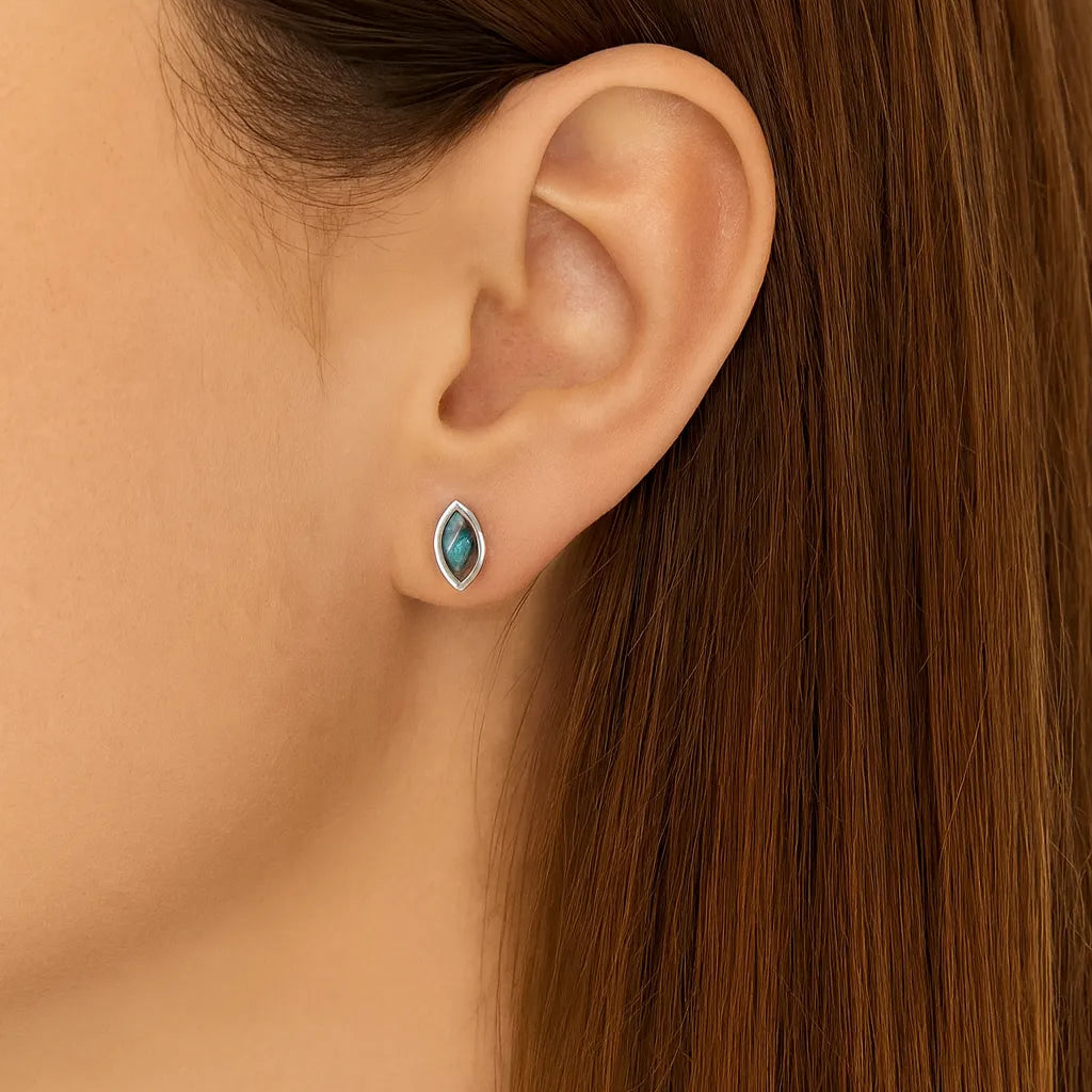 Nahaufnahme eines Ohres mit einem eleganten Ohrstecker in Marquiseform aus 925er Sterlingsilber, gefasst mit einem schimmernden Labradorit-Cabochon, der in Blau- und Grautönen irisierend leuchtet. Der Ohrstecker wirkt dezent und edel am Ohr getragen.