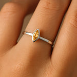 Eine Nahaufnahme einer Frauenhand zeigt einen eleganten Silberring am Ringfinger. Der Ring trägt einen 5 mm langen, facettierten, tropfenförmigen Citrin in einem warmen Goldgelbton. Der Fokus liegt klar auf dem Ring, dessen zarte Ringschiene und feiner Glanz den leuchtenden Stein harmonisch hervorheben. Der Hintergrund ist neutral und weichgezeichnet, um den Ring in den Mittelpunkt zu stellen.
