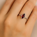 
Ein realistisches Nahaufnahmefoto zeigt die linke Hand einer Frau, die einen eleganten Silberring mit einem marquisförmigen, rot funkelnden Granatstein am Ringfinger trägt. Der Ring liegt dezent auf der Haut, der Fokus liegt klar auf dem facettierten Edelstein und seiner glänzenden Fassung.
