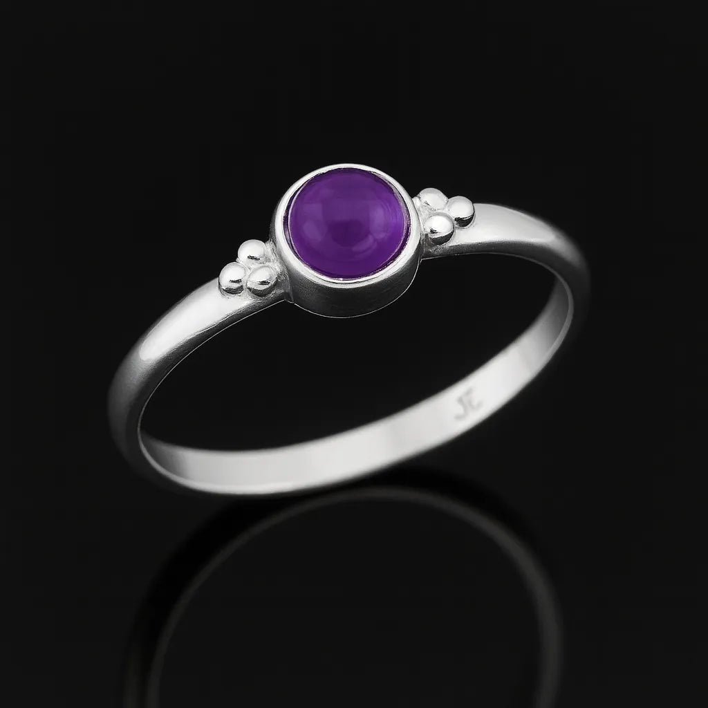 Silberring mit rundem violettem Amethyst, liegend auf schwarzem spiegelndem Untergrund, edles Schmuckproduktfoto mit starker Reflexion und seitlicher Perspektive.