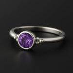 Silberring mit 4 mm rund facettiertem violettem Amethyst in Zargenfassung, Damenring aus 925 Sterling Silber mit Kugel-Details, edel präsentiert auf schwarzem Hintergrund.
