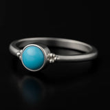 Damenring aus Sterling Silber mit rundem blauem Chalcedon Cabochon (4 mm) in Zargenfassung – filigraner Silberring mit hellblauem Edelstein, edel inszeniert auf schwarzem Hintergrund mit Spiegelung.
