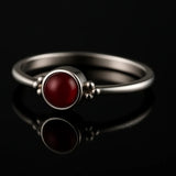 Eleganter Damenring aus 925 Sterling Silber mit rundem Granat-Cabochon (tiefrot) in Zargenfassung und feinen Silberkugeln, edel präsentiert auf schwarzem spiegelnden Hintergrund als hochwertiger Edelsteinschmuck.
