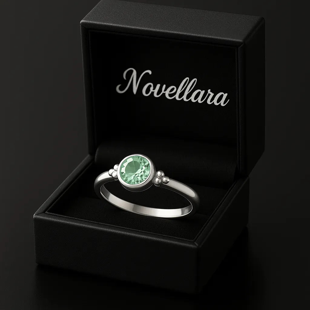 Eleganter Silberring mit rund facettiertem grünem Edelstein (4 mm) in Zargenfassung, präsentiert in geöffneter schwarzer Schmuckbox mit Novellara Logo – hochwertiger Damenring als Geschenk oder Verlobungsring.
