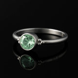 Silberring mit rund facettiertem grünem Edelstein (4 mm) in Zargenfassung, Damenring aus 925 Sterling Silber mit Kugel-Details, edel inszeniert auf schwarzem spiegelnden Hintergrund als hochwertiger Schmuck.
