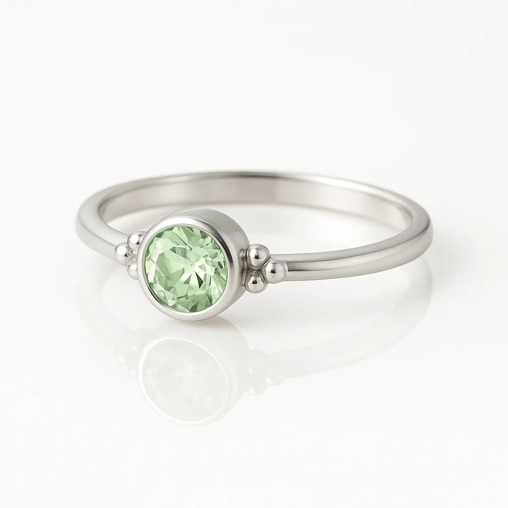 Eleganter Damenring aus 925 Sterling Silber mit rund facettiertem hellgrünem Edelstein (4 mm) in Zargenfassung und feinen Silberkugeln, edel fotografiert auf weißem spiegelnden Hintergrund als hochwertiger Schmuck.
