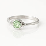 Eleganter Damenring aus 925 Sterling Silber mit rund facettiertem hellgrünem Edelstein (4 mm) in Zargenfassung und feinen Silberkugeln, edel fotografiert auf weißem spiegelnden Hintergrund als hochwertiger Schmuck.
