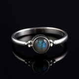 Damenring aus Sterling Silber mit rundem Labradorit Cabochon (4 mm) in Zargenfassung – feiner Silberring mit schimmernd blau-grauem Edelstein, edel präsentiert auf schwarzem spiegelnden Hintergrund.
