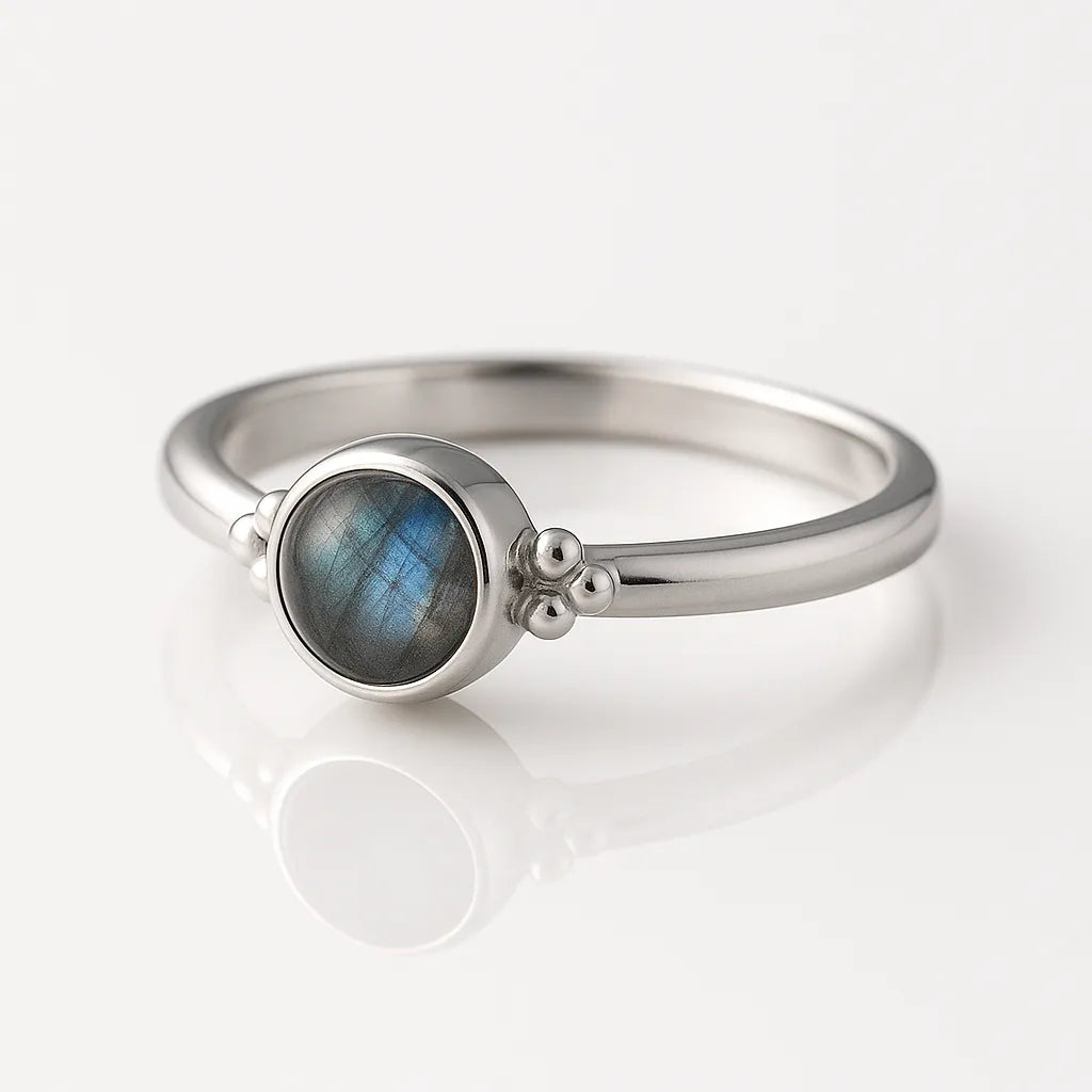 Damenring aus Sterling Silber mit rundem Labradorit Cabochon (4 mm) in Zargenfassung – eleganter Silberring mit blau-grün schimmerndem Edelstein, fotografiert seitlich auf weißem spiegelnden Hintergrund als exklusiver Damenschmuck.
