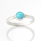 Silberring mit rundem Larimar-Cabochon in Zargenfassung, liegend auf hellem spiegelnden Untergrund mit klarer Reflexion, hochwertige Schmuck Nahaufnahme für Produktdarstellung.