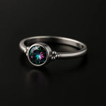"Feiner Damenring aus mattiertem Silber mit rundem facettiertem Mystic Topas in Grün-Lila Schimmer, Zargenfassung und Kugeldetails – eleganter Silberring auf schwarzem Hintergrund"
