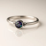 Zarter Damenring aus poliertem Silber mit rundem facettiertem Mystic Topas in Grün-Lila Schimmer, Zargenfassung und Kugeldetails – eleganter Silberring mit Edelstein auf hellem Hintergrund