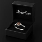 `Eleganter Silberring mit rund facettiertem Rauchquarz Stein (4 mm) in Zargenfassung, präsentiert in einer geöffneten schwarzen Schmuckbox mit Novellara Logo im Deckel – edles Damenschmuck Geschenk.`
