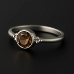 Damenring aus Sterling Silber mit rundem facettierten Rauchquarz in Zargenfassung – filigraner Silberring mit braunem Edelstein auf schwarzem spiegelnden Hintergrund, eleganter Schmuck für Frauen.
