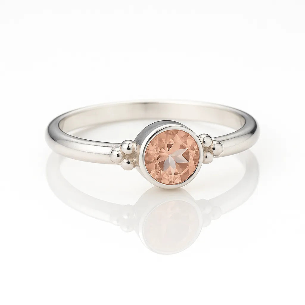 Feiner Damenring aus 925 Silber mit facettiertem apricotfarbenem Zirkonia-Stein und dekorativen Silberkügelchen, seitlich fotografiert auf hellem reflektierendem Hintergrund als edles Produktfoto für Schmuck.