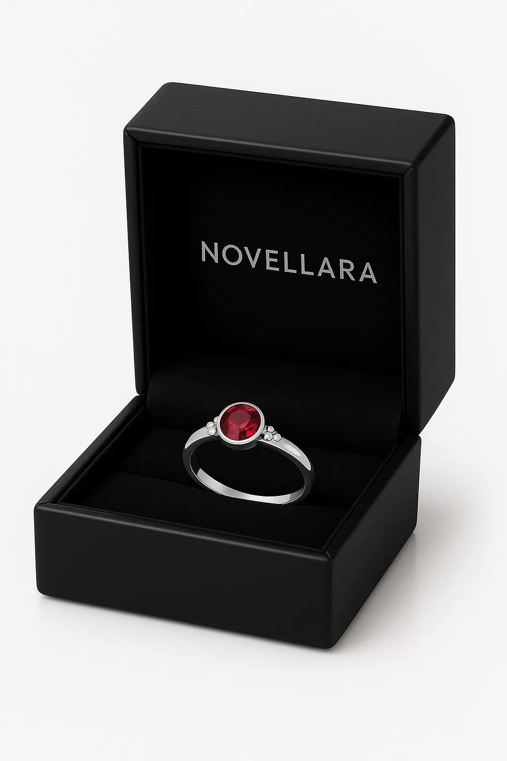 Ein silberner Ring mit einem runden, roten 4-mm-Stein liegt in einer offenen, schwarzen Schmuckschatulle mit Samteinlage. Auf der Innenseite des Deckels ist das Logo „NOVELLARA“ in heller Schrift zu sehen. Das Bild ist in hoher Studioqualität vor hellem Hintergrund aufgenommen.