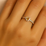 Nahaufnahme einer Frauenhand mit einem eleganten Silberring am Ringfinger. Der Ring besitzt einen dreieckigen, facettierten Citrinstein in warmem Goldgelb, der in einer glatten Zargenfassung sitzt. Das Licht spiegelt sich dezent auf der glänzenden Ringschiene, wodurch der klare, moderne Stil des Schmuckstücks betont wird. Der Fokus liegt deutlich auf dem Ring, während die Hand einen natürlichen Hautton aufweist und weich beleuchtet ist.
