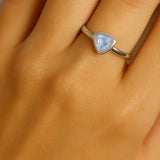 Eine Nahaufnahme einer Frauenhand zeigt einen eleganten Silberring am Ringfinger. Der Ring besitzt eine schlichte, glatte Ringschiene und ist mit einem dreieckig facettierten, hellblauen Blautopas von etwa 5 mm Länge besetzt. Der Fokus liegt klar auf dem Ring und seinem funkelnden Edelstein, während die Haut im Hintergrund weich und natürlich wirkt.
