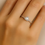 Eine Nahaufnahme zeigt die linke Hand einer Frau mit einem eleganten Silberring am Ringfinger. Der Ring besitzt eine zarte, dreieckige Fassung mit einer kleinen weißen Perle in der Mitte. Der Fokus liegt auf dem Ring, während die Haut der Hand weich und natürlich beleuchtet ist.
