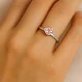 Nahaufnahme einer Frauenhand, die einen eleganten Silberring am Ringfinger trägt. Der Ring hat eine schmale, glänzende Ringschiene und ist mit einem zart roséfarbenen, dreieckig facettierten Rosenquarz besetzt. Der Fokus des Bildes liegt auf dem Ring und dem Edelstein, während die Haut sanft beleuchtet ist und den Schmuck dezent hervorhebt.
