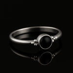 Eleganter 925-Silberring mit poliertem schwarzem Onyx-Stein im Cabochon-Schliff, seitlich fotografiert auf glänzend schwarzem Spiegelhintergrund mit starker Reflexion, hochwertiges Schmuck-Produktfoto.
