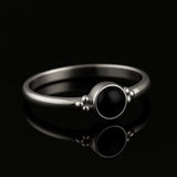 Eleganter 925-Silberring mit poliertem schwarzem Onyx-Stein im Cabochon-Schliff, seitlich fotografiert auf glänzend schwarzem Spiegelhintergrund mit starker Reflexion, hochwertiges Schmuck-Produktfoto.