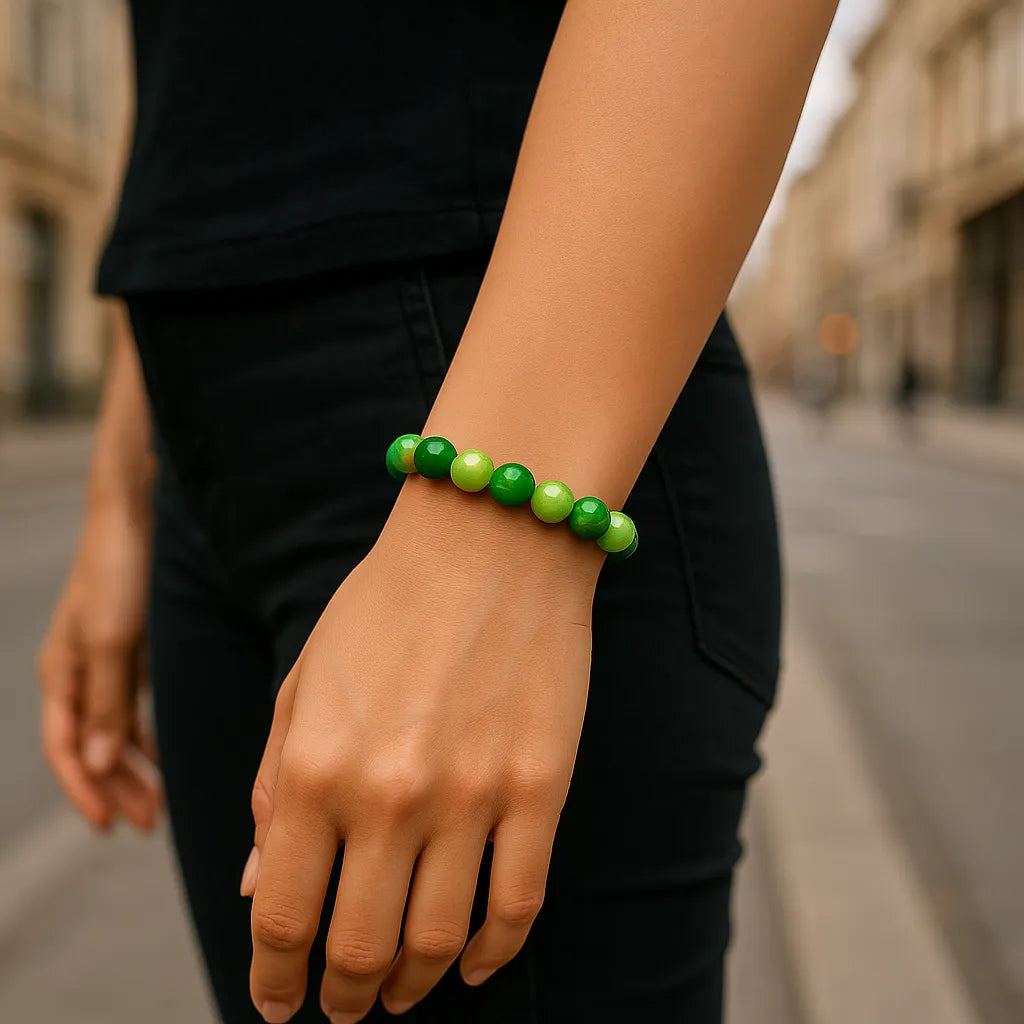 Eine Person trägt ein Armband aus großen, glänzenden grünen Perlen, während sie auf einer städtischen Straße steht. Die Person trägt schwarze Kleidung, der Fokus liegt auf dem Handgelenk und dem Armband.