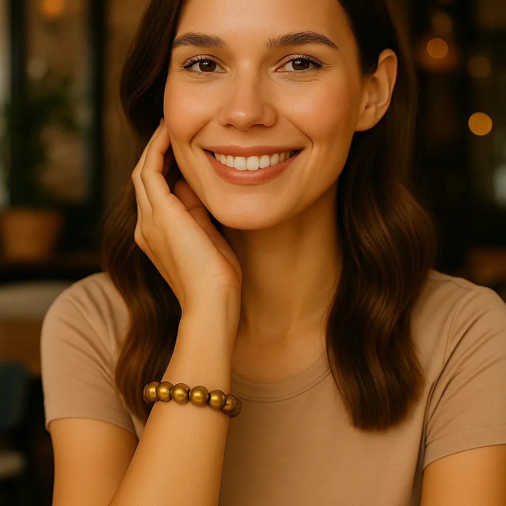 Eine junge Frau sitzt freundlich lächelnd in einem Café. Sie trägt ein goldenes Perlenarmband am Handgelenk, das elegant zur natürlichen Atmosphäre passt.