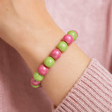 Nahaufnahme eines Handgelenks, das ein Armband aus abwechselnd pinken und grünen Perlen trägt. Die Person trägt einen hellrosa Strickpullover.